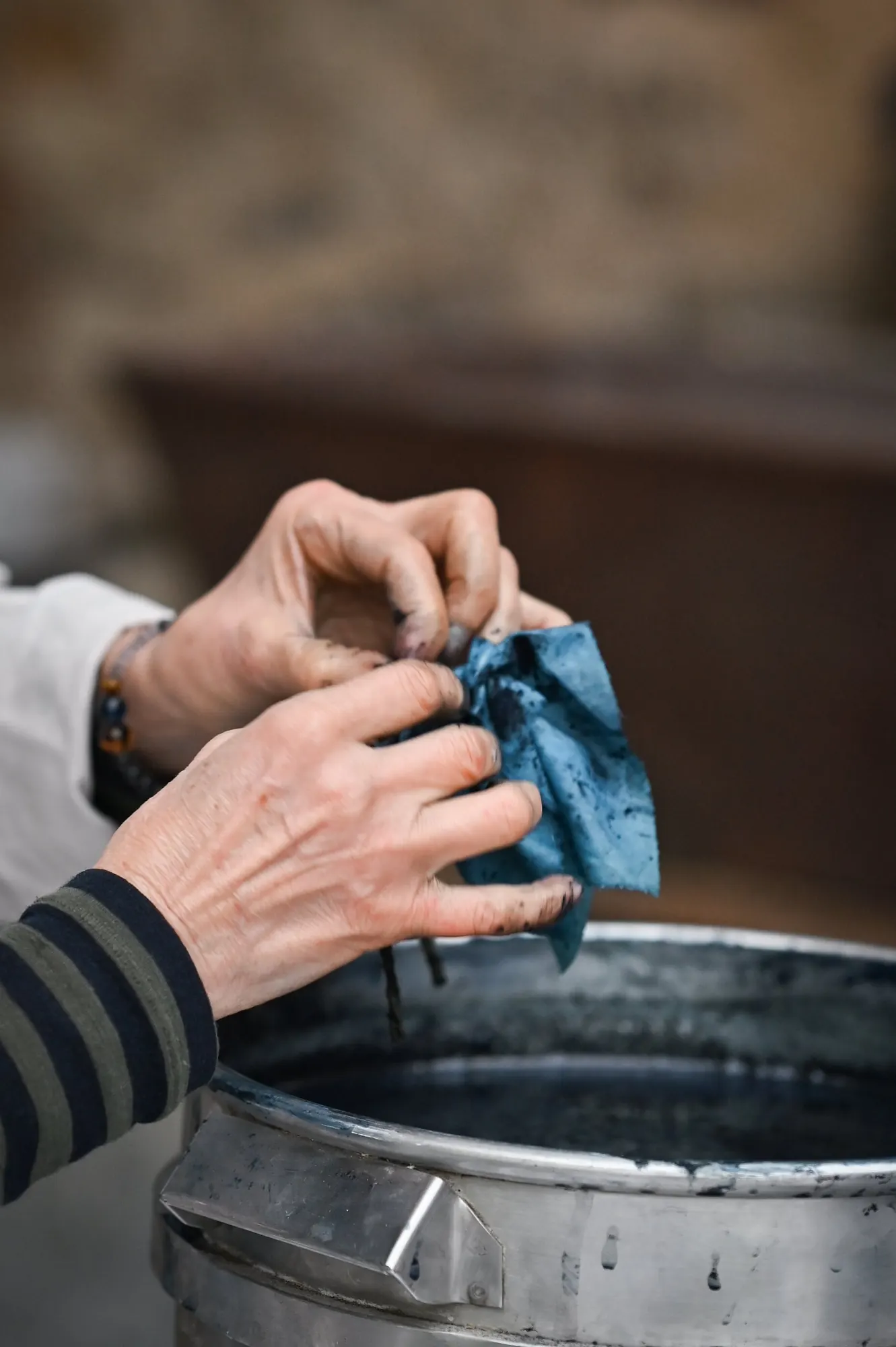 Hands lifting a blue-dyed cloth from a dye vat