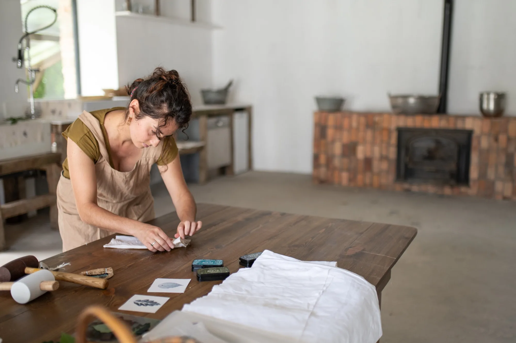 Une artisane imprime un motif de feuille sur un tissu blanc, sur la grande table en bois de l’atelier de la Manufacture du Blanc