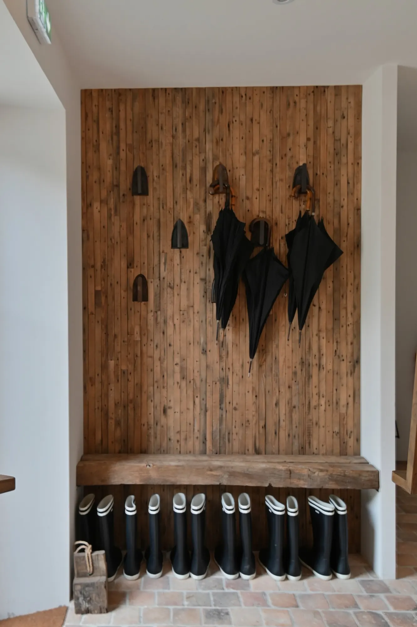 Rubber boots, umbrellas and a wooden bench by the entrance