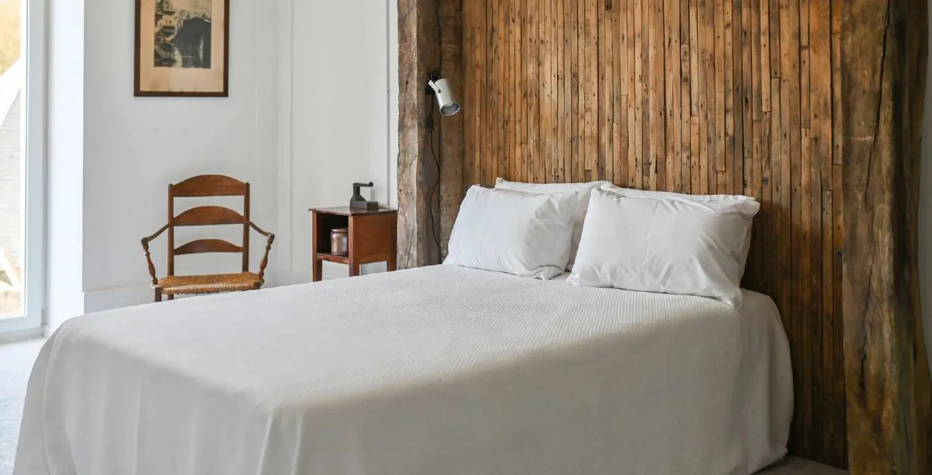 A bedroom with white linen and an old timber headboard