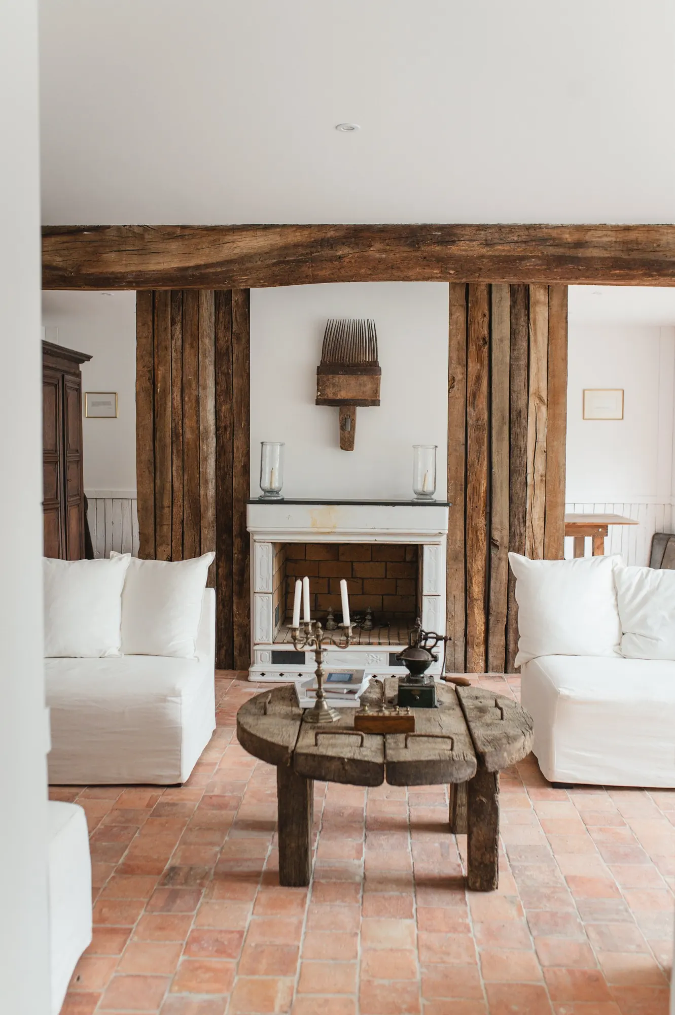 A sitting room with white sofas, oak beams and a fireplace with candles